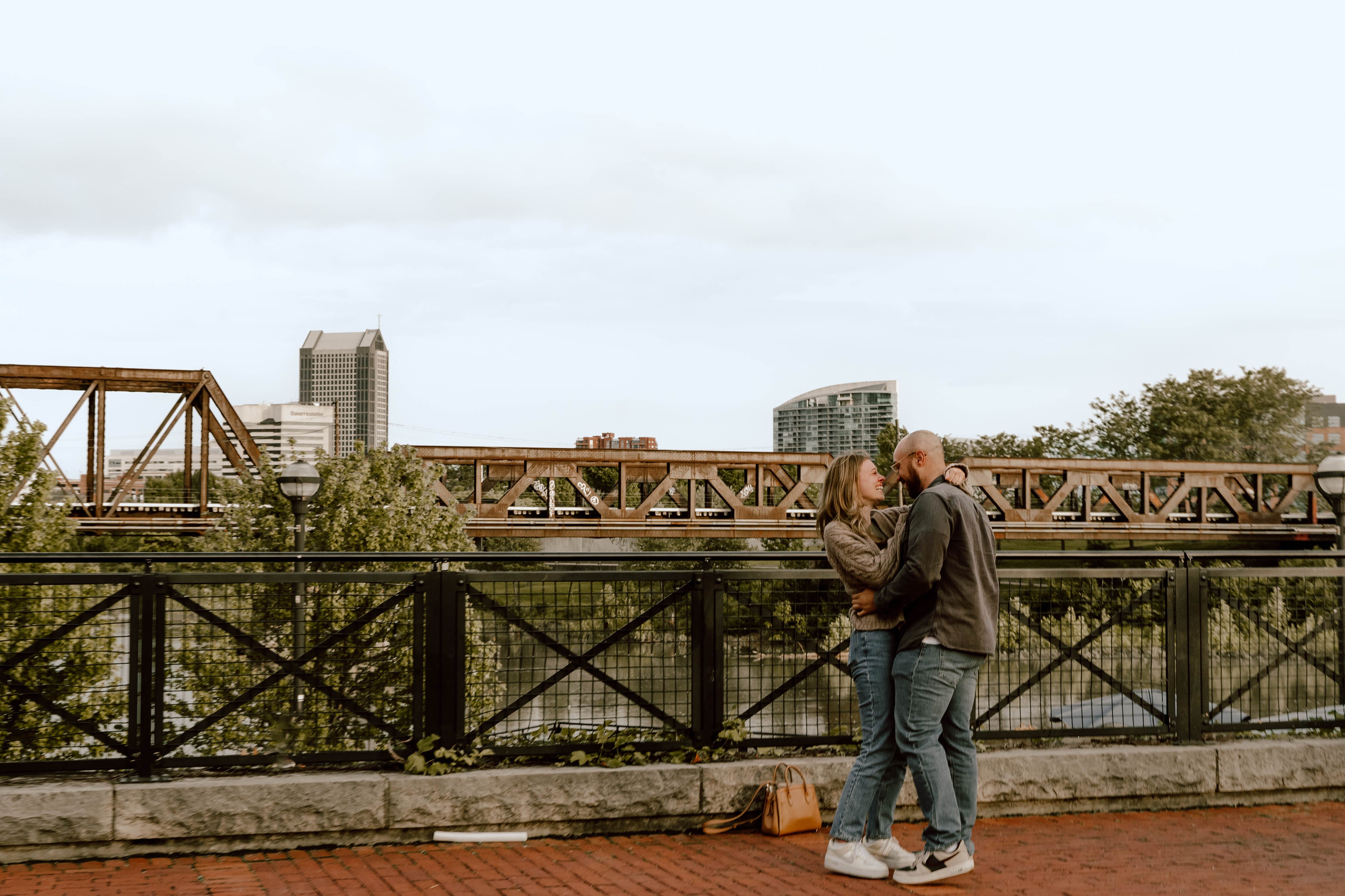 Andrew and Chloë embracing with a scenic bridge in the background.